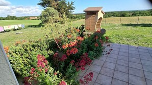 A garden area with a stone structure, various flowering plants, and a view of a distant field. - Spacious Farmhouse with Wi-Fi, Terraces, and Lake Access (Brem)