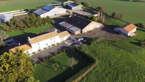 A rural property with multiple buildings, including a large white house with a tiled roof, a smaller building with a green roof, and several barns. There are open fields and wind turbines in the background. - Spacious Farmhouse with Wi-Fi, Terraces, and Lake Access (Brem)