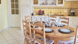 A dining area with a wooden table set for four, surrounded by chairs. There is a kitchen area with white cabinets and a yellow-tiled backsplash. - Spacious Farmhouse with Wi-Fi, Terraces, and Lake Access (Brem)