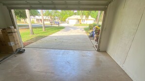 A garage with a concrete floor, a partially open door, and cardboard boxes on the left.