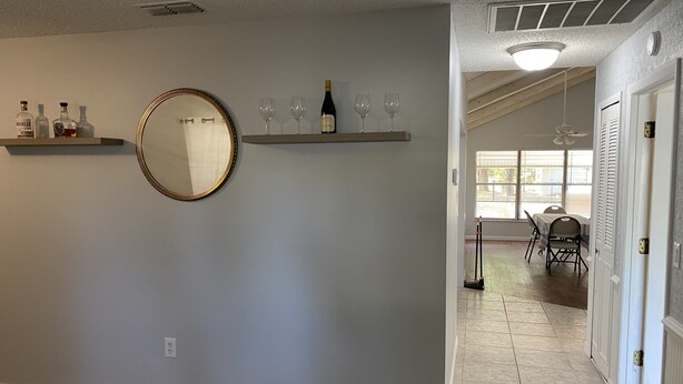 A hallway with a mirror, shelves with bottles, and a dining area in the background.
