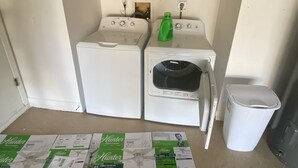 A compact laundry room with two washing machines, a dryer, and a small shelf above.