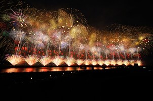 Espectáculo de fuegos artificiales nocturnos sobre un cuerpo de agua, con reflejos en la superficie.