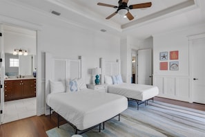 A bedroom with two beds, a ceiling fan, a bathroom with a vanity, and a hallway with a door.