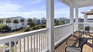 A covered balcony with a view of a residential area, including houses and palm trees.