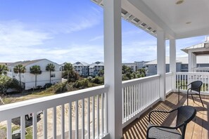 A covered balcony with a view of a residential area, including houses and palm trees.