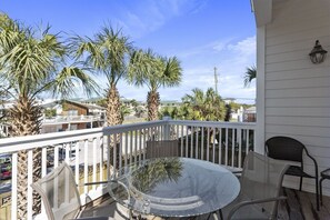 A balcony with a glass table and chairs, surrounded by palm trees and a white railing.