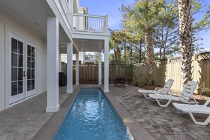 A swimming pool with a covered patio area, outdoor furniture, and a wooden fence.