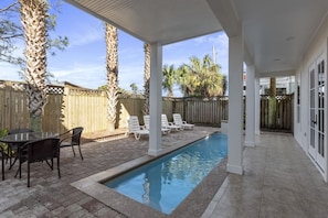 A covered outdoor swimming pool area with lounge chairs and a table.