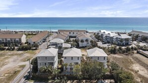A coastal residential area with multiple two-story houses, a beach in the background, and a clear sky.