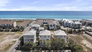 A coastal residential area with multiple two-story houses, a beach in the background, and a clear sky.