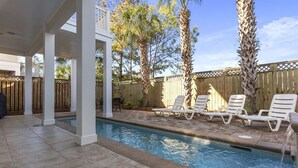 A swimming pool with lounge chairs and a wooden fence in the background.