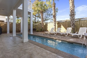 A swimming pool with lounge chairs and a wooden fence in the background.