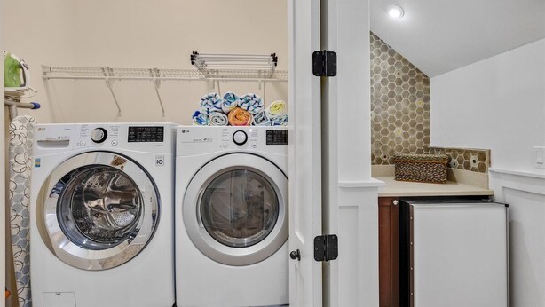 A laundry area with two front-loading washing machines, a drying rack, and a small refrigerator.