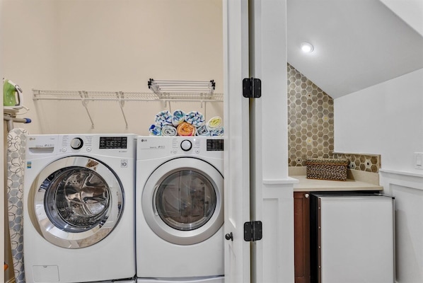 A laundry area with two front-loading washing machines, a drying rack, and a small refrigerator.