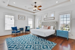 A bedroom with a tufted headboard, a patterned rug, and a ceiling fan.