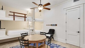A compact room with bunk beds, a ceiling fan, a small dining table with chairs, and a white door.