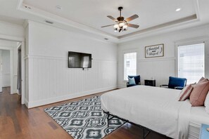 Quarto com cama grande, ventilador de teto, televisão de tela plana e um letreiro decorativo.