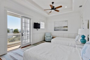 A bedroom with two beds, a ceiling fan, a television, and a balcony with a view.