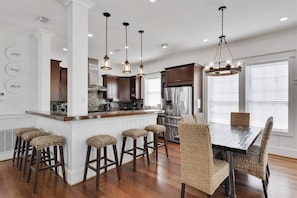 A modern kitchen with a central island, bar stools, and a dining table with wicker chairs.