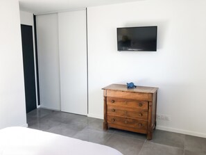 Een slaapkamer met een bed, een houten dressoir, een aan de muur bevestigde televisie en een schuifdeur.