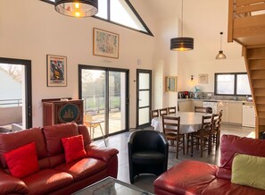 A spacious living area with leather sofas, a dining table, and a kitchen in the background.