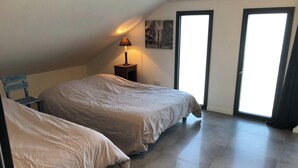 A bedroom with two beds, a nightstand with a lamp, a framed picture on the wall, and a sliding glass door. - Homerez - House in Baden (Baden)