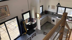 A modern kitchen with a built-in washer and dryer, a dining area with a round table, and a staircase leading to an upper level. - Homerez - House in Baden (Baden)