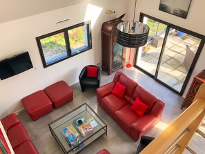 A spacious living area with a large window, a red sofa, a glass coffee table, and a television.