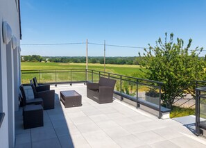 Een balkon met buitenmeubilair, een glazen hekwerk en uitzicht op een groen landschap.