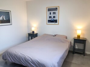 A bedroom with a bed, two bedside tables, two wall-mounted lamps, and a framed picture on the wall.