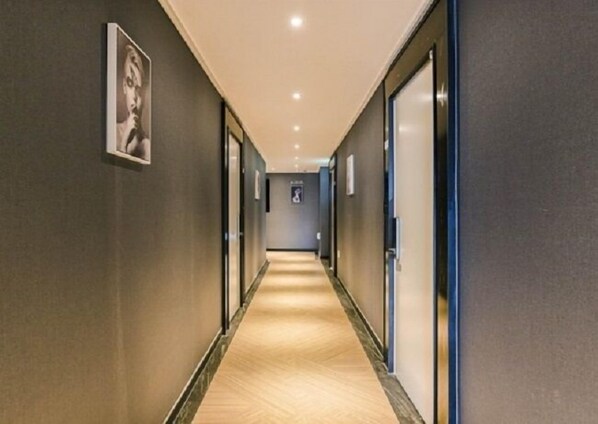 A long, narrow hotel corridor with a carpeted floor, dark walls, and doors on both sides.