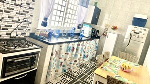 Eine kompakte Küche mit Gasherd, Backofen, Mikrowelle und Kühlschrank. Es gibt einen Esstisch mit Stühlen und eine Obstschale.