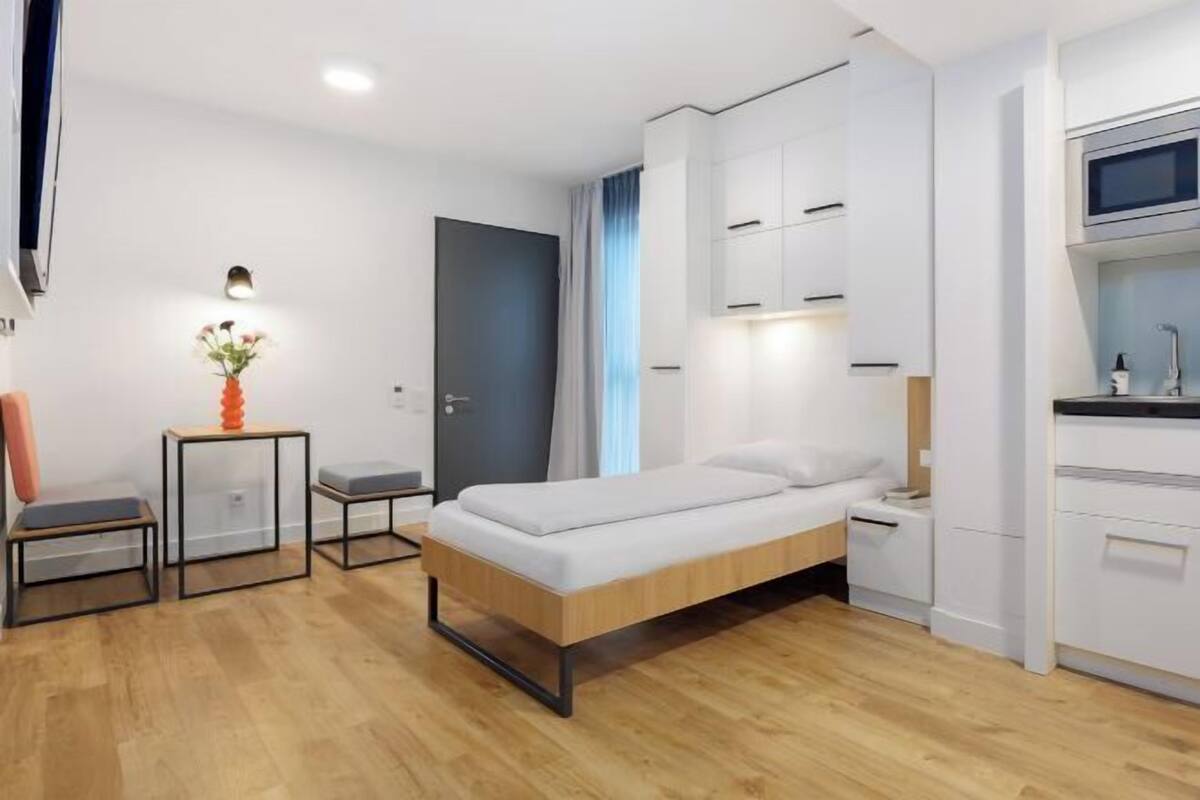 Une chambre moderne comprenant un lit, des tables de chevet, un petit bureau avec une chaise et un coin cuisine.