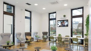 Een moderne lounge met comfortabele zitmogelijkheden, een lange tafel en grote ramen met uitzicht op de omgeving.