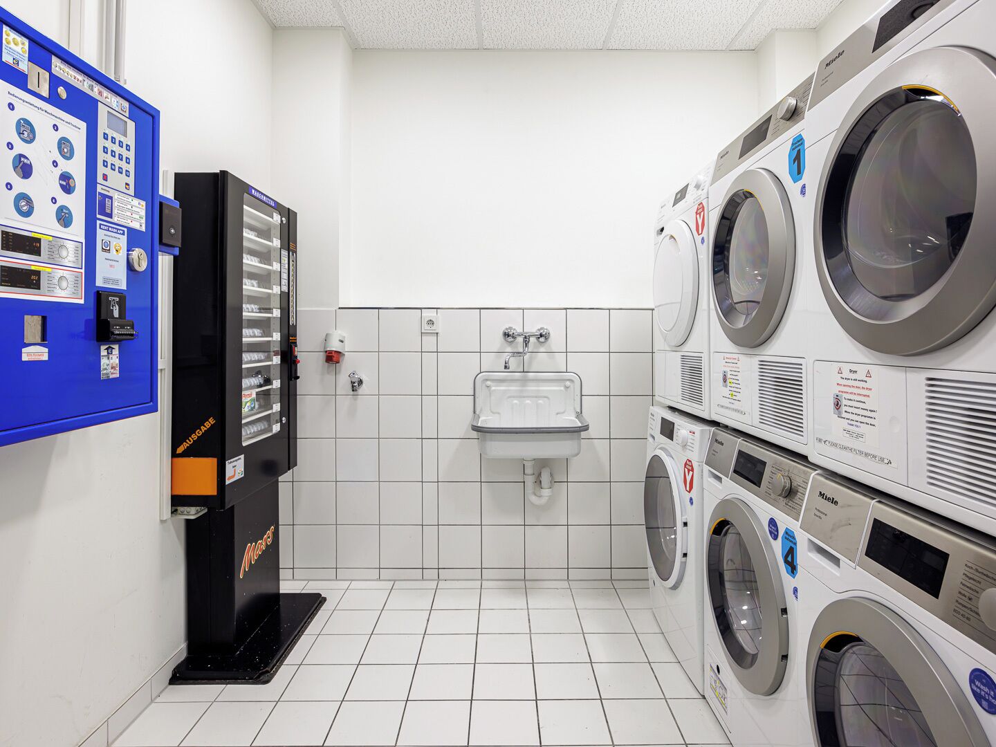 A laundry facility with a control panel, a sink, and stacked washing machines.