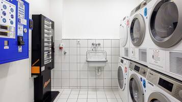 A laundry facility with a control panel, a sink, and stacked washing machines.