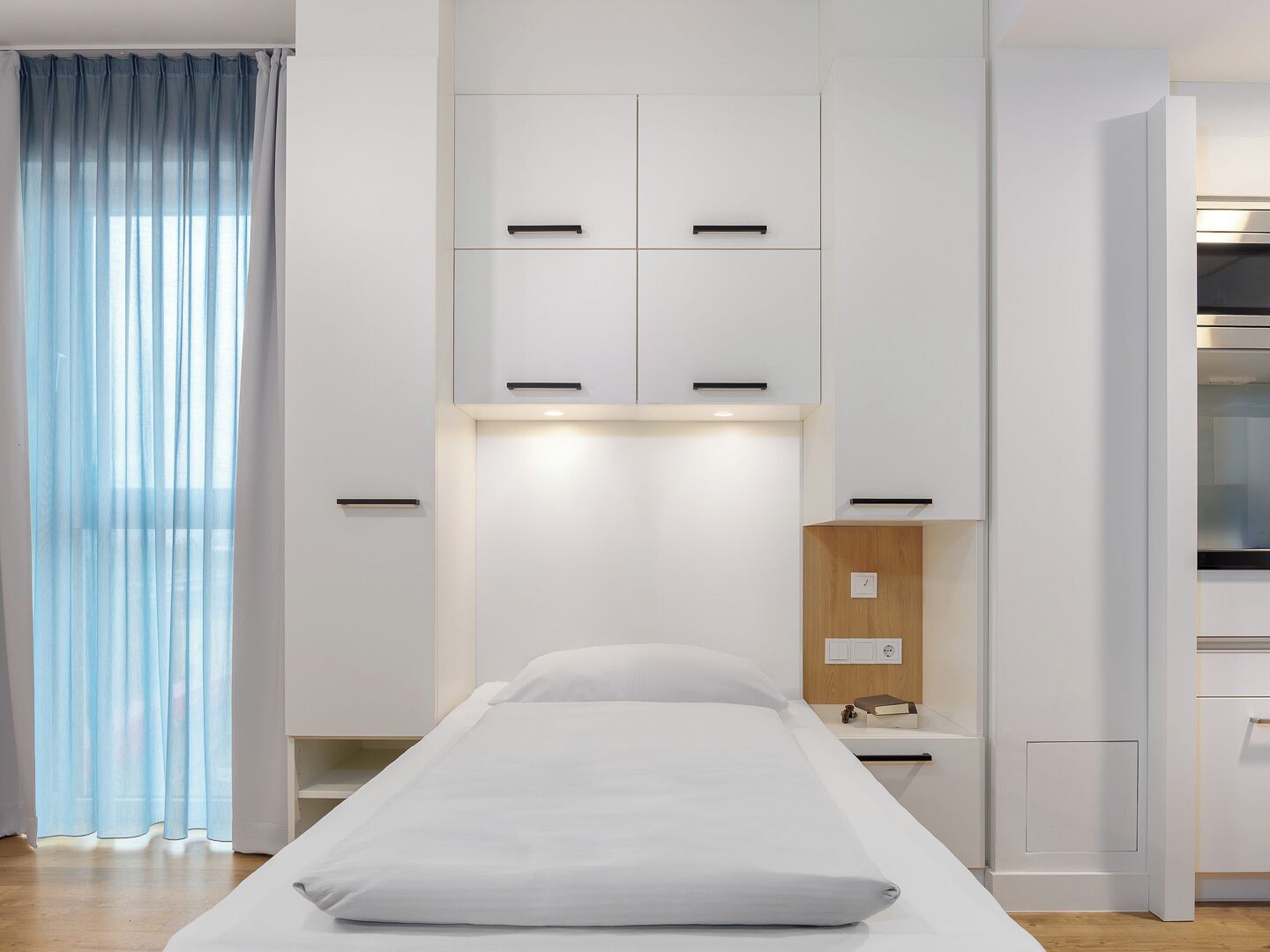 Quarto minimalista com cama, guarda-roupa branco e mesa de cabeceira de madeira.