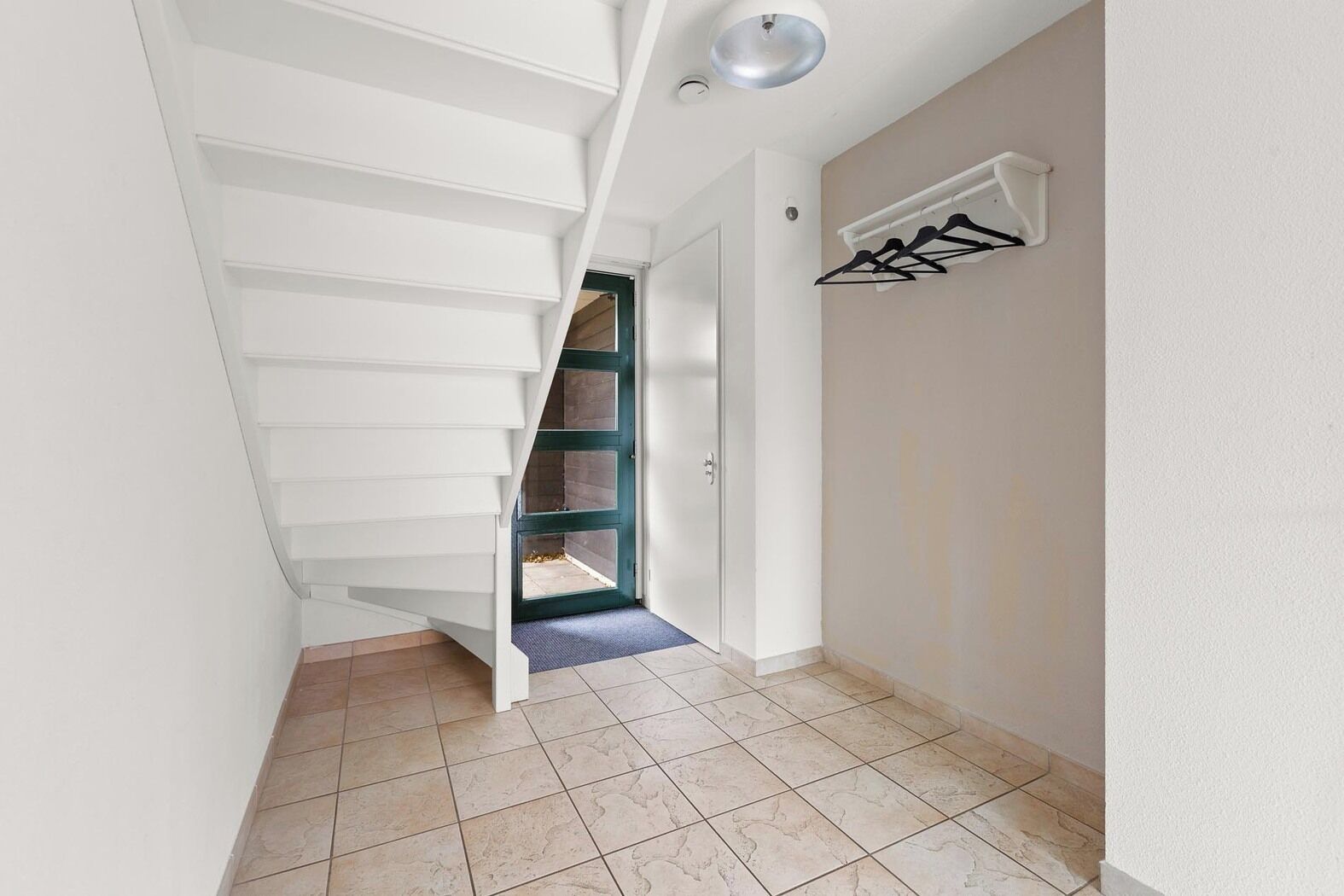 A narrow hallway with a white staircase leading to a door.