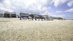 Een strand met gebouwen op de achtergrond, waaronder een groot hotel en een kleinere constructie.