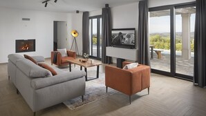 A modern living room with a fireplace, a television, and a view of a pool and landscape. - Lovely Villa Arman with a pool and a jacuzzi (Vizinada)