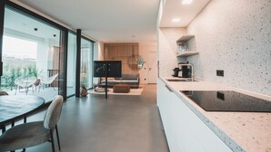 A modern kitchen with a large island, a dining area with a round table and chairs, and a living area with a sofa and a TV. - Modern Villa "Montelino Boutiquehouse " with Pool, Wi-Fi, Air Conditioning & Terrace (Bardolino)