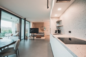 A modern kitchen with a large island, a dining area with a round table and chairs, and a living area with a sofa and a TV.