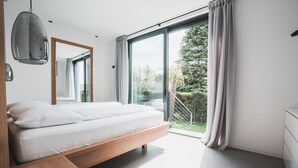 A modern bedroom with a large bed, a wooden bedside table, a hanging pendant light, a large mirror, and a sliding glass door leading to a balcony with a view of greenery. - Modern Villa "Montelino Boutiquehouse " with Pool, Wi-Fi, Air Conditioning & Terrace (Bardolino)
