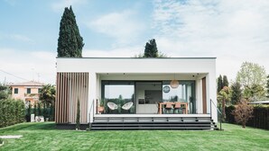 A modern house with a large glass window, a wooden deck, and a well-maintained lawn. - Modern Villa "Montelino Boutiquehouse " with Pool, Wi-Fi, Air Conditioning & Terrace (Bardolino)