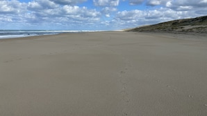 Una playa amplia y vacía con huellas que se adentran en el océano bajo un cielo parcialmente nublado.
