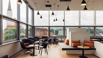 Un café moderne avec de grandes fenêtres, des chaises noires, des tables rondes et une vue sur le clocher d’une église.