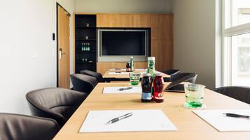 A conference room with a long table, chairs, a projector screen, and a shelf with bottled beverages.