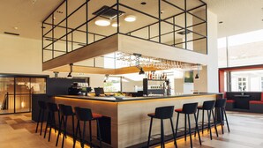 A modern bar area with a central island, bar stools, and a high ceiling with exposed beams. - harry’s home Steyr hotel & apartments (Steyr)