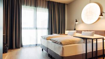 A modern hotel room with a large bed, a bedside table, and a wall-mounted light fixture.